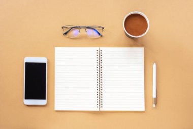 Boş not defteri, kalem, kağıt bardakta kahve, akıllı telefon ve bej masadaki bardaklar. Üst görünüm, düz görünüm, maket