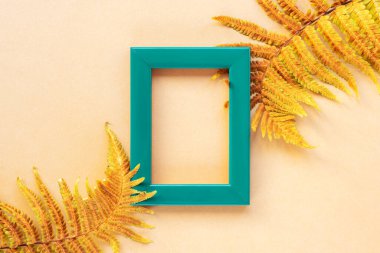 Yeşil çerçeve ve sarı eğrelti otu yaprakları bej arka planda. Üst manzara, düz yatış. Model
