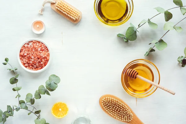 Ev yapımı fırça için doğal malzemeler. Yağ, bal, pembe himalaya tuzu, yüz veya vücut fırçası, limon ve okaliptüs dalları beyaz ahşap masa üzerinde. Üst görünüm, düz görünüm, kopyalama alanı.