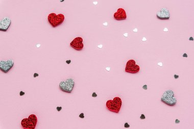 Kırmızı ve gümüş parıldayan kalpler pembe arka planda konfeti ile. Sevgililer Günü konsepti. Doku, arkaplan.