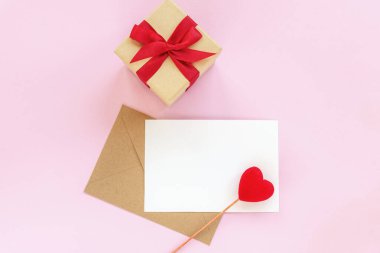 Üzerinde kırmızı kalp ve hediye kutusu olan boş bir kağıt ve zarf. Pembe arka plan, üst manzara, düz yatak, maket. Sevgililer Günü konsepti, 14 Şubat.