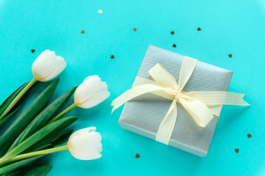 Hediye kutusu ve beyaz laleler konfetiyle mavi arka planda. Doğum günü, kadınlar günü, anneler günü, sevgililer günü konsepti. Üst görünüm.