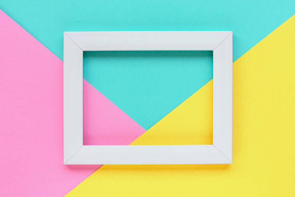 Blank picture frame on three toned pink, blue and yellow background . Spring holidays concept. Top view, flat lay, mockup.