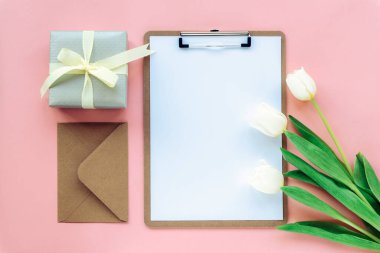 Beyaz laleli, hediye kutusu ve zarflı pembe arka planda bir pano modeli. Kadınlar günü konsepti. Üst görünüm, düz görünüm, kopyalama alanı.