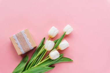 Hediye kutusu ve pembe arka planda bir buket beyaz lale. Kadınlar günü, anneler günü, bahar konsepti. Üst görünüm, düz görünüm, kopyalama alanı