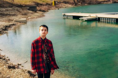 Nehir kıyısında kısa saçlı, günlük kıyafetli genç bir kız duruyor.