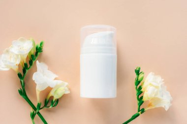 Kozmetik beyaz boş şeker şişesi ve bej arka planda frezya çiçekleri. Doğal kozmetik konsepti. Üst görünüm, düz görünüm, maket.