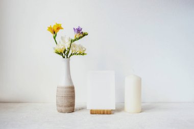 Boş kağıt, mum ve bir buket beyaz, sarı ve mavi frezya çiçekleri beyaz arka planda vazoda. Ev dekoru, maket yap.
