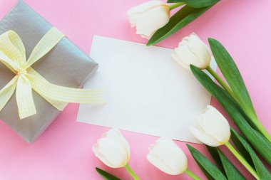 Boş çarşaf, hediye kutusu ve pembe arka planda beyaz laleler. Kadınlar Günü, Anneler Günü konsepti. Üst görünüm, düz görünüm, model.