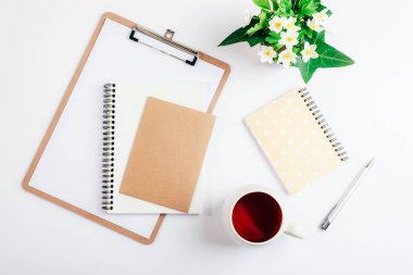 Beyaz pano, bir fincan çay, defterler, kalem ve bir buket bahar çiçeği. Üst görünüm, düz görünüm, model.