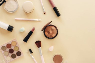 Düz makyaj, cilt temeli, ruj, göz farı paleti, pudra ve güzellik aksesuarları. Pastel bej arka planda kozmetik güzellik ürünleri. Üst görünüm.