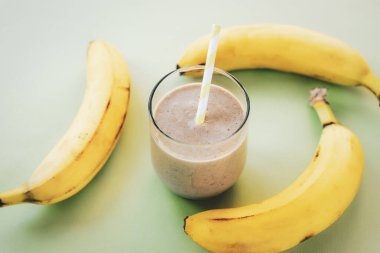 Bardakta protein kokteyli ve açık yeşil arka planda muz, yakın plan. Sağlıklı yemek..