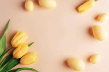 Tarafsız bej arka planda sarı süslemeli paskalya yumurtası ve lale çerçevesi. Üst görünüm, düz görünüm, kopyalama alanı.