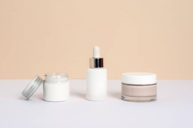 Kavanozda krem, serum şişesi ve yüz maskesi ya da tarafsız bej ve beyaz bir arka plan. Doğal cilt bakım ürünleri, modelleme