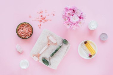 Sakura çiçekli doğal organik kaplıca seti. Düz banyo tuzu, yüz silindirleri, kiraz çiçekleri, pembe arka planda kozmetik krem ve yağ. Cilt bakımı, güzellik tedavi konsepti