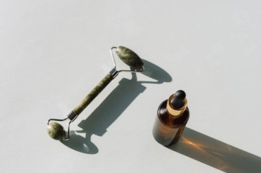 Serum şişesi ve yeşil yüz silindiri açık mavi arka planda, sert gölgeli. Üst görünüm, düz görünüm, kopyalama alanı