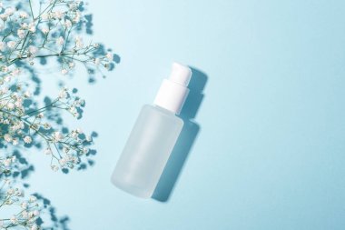 Açık mavi arka planda beyaz çigila çiçekli serum şişesi. Alternatif tıp, güzellik ürünleri. Üst görünüm, düz görünüm, kopyalama alanı