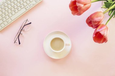 Klavyesi, lale çiçekleri, kahve fincanı ve bardakları olan pembe kadın işyeri. Bahar tatili, anneler günü konsepti. Üst manzara, düz uzanma