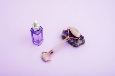 Ametist kristal ve mor serum şişesinde yüz silindiri. Nemlendirici ve cilt bakım aletleri. Spa ve sağlık konsepti. Üst görünüm.