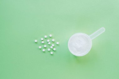Kolajen tozu ve yeşil arka planda C vitamini tabletleri. Kolajen üretimini destekleyen takviyeler. Üst görünüm, düz görünüm, kopyalama alanı.