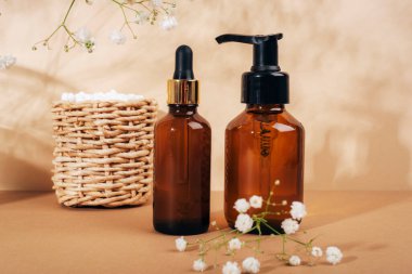 Kozmetik yüz temizleyici ve serum kahverengi cam şişeler sepette kulak çubukları ve açık bej arka planda çingene beyaz çiçekler. Doğal kozmetik, spa ve sağlık konsepti. Kapat..