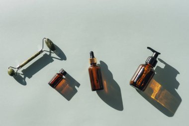 Yüz temizleyicisi, serum şişesi, temel yağ ve açık mavi arka planda yeşil yüz silindiri, koyu gölgeler, üst görüş. Düz yat, boşluğu kopyala