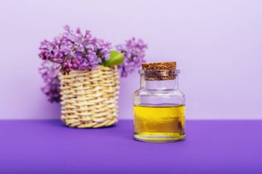 Kavanozda kozmetik yağı ve mor arka planda leylak çiçekleri. Aromaterapi, cilt bakımı. Seçici odak.