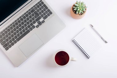 Dizüstü bilgisayarı, çay fincanı, not defteri ve sulu beyaz işyeri. Merkez ofis, iş konsepti. Üst manzara, düz uzanma.