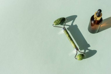 Serum şişesi ve yeşil yüz silindiri açık mavi arka planda, sert gölgeli. Üst görünüm, alanı kopyala.