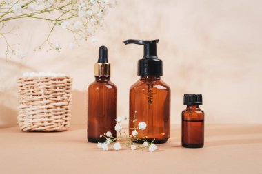 Kozmetik yüz temizleyici, serum kahverengi cam şişeler, esaslı yağ ve açık bej arka planda çingene beyaz çiçekleri. Doğal kozmetik, spa ve sağlık konsepti. Seçici odak.
