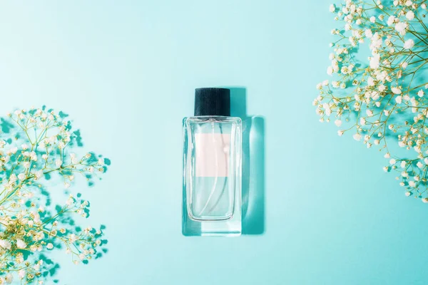 Açık mavi arkaplanlı parfüm şişesi ve çingene çiçekleri. Güzellik, moda konsepti. Üst manzara, düz uzanma.