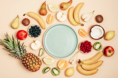 Sarı arka planda çeşitli meyveler, ortada mavi bir plaka. Üst manzara, düz yatış, maket. Tropik meyveler, vejetaryen yiyecekler, sağlıklı beslenme.