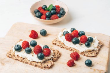Beyaz ahşap masada böğürtlenli ve ahududulu sandviçler. Sağlıklı kahvaltı. Üst görünüm.