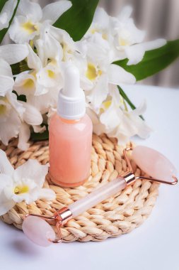 Pembe serum şişesi ve büyük beyaz çiçekli gül kuvars yüz silindiri. Güzellik, kaplıca ve sağlık konsepti. Yakın çekim..