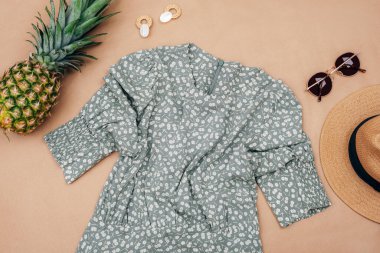 Şık kadın kıyafetleri ve aksesuarları. Yazlık elbise, güneş gözlüğü, hasır şapka ve bej arka planda ananas. Düz yatış, üst görünüm.