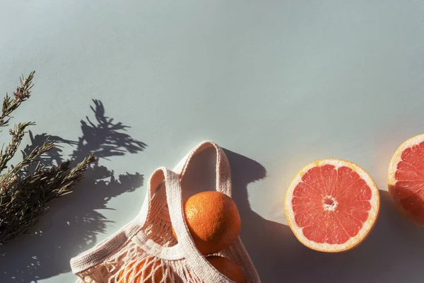 Fresh red grapefruit, mesh bag and herbs in sunlight. Top view, flat lay, copy space.