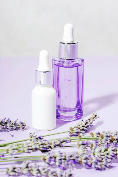 Skincare products, serum and cosmetic oil and lavender blossom on light purple background. Aromatherapy and natural cosmetics concept. Closeup.