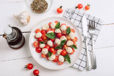 Kiraz domatesli İtalyan caprese salatası, mozzarella, fesleğen, sarımsak, beyaz bir masada balzamik sos. Üst manzara, düz uzanma.