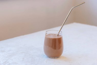 Sağlıklı protein çikolatalı smoothie beyaz masada metal pipet ile, yakın çekim.