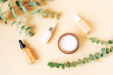 Kozmetik şişeler, aroma mumu ve bej arka planda okaliptüs dalları. Doğal kozmetik ürünleri, aromaterapi ve cilt bakımı konsepti. Üst manzara, düz uzanma.