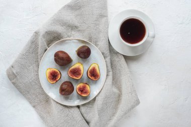 Kahve fincanı ve beyaz desenli masa üzerindeki incirlerle dolu bir hayat. Üst manzara, düz uzanma.