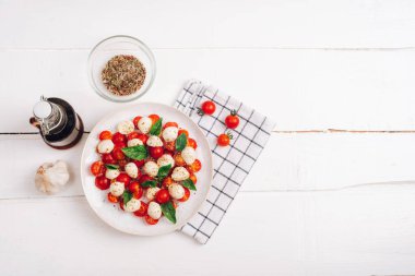 Kiraz domatesli İtalyan caprese salatası, mozzarella, fesleğen, sarımsak, beyaz ahşap masadaki balzamik sos. Üst görünüm, düz görünüm, kopyalama alanı.