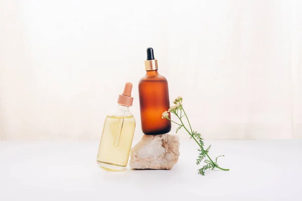 Two cosmetic oil or serum bottles on a stone and yarrow flower on white background. Natural cosmetics, spa and wellness concept.