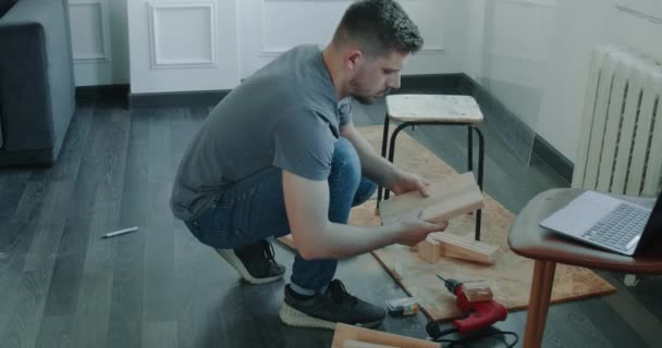 O homem está construindo móveis ele mesmo fazendo renovação em casa. Homem está procurando instrução no computador. — Vídeo de Stock
