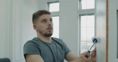 Tamir işleri. Bir adam silindirle duvar boyuyor. Bir adam onarımlar yapar. Odada tamirat yapan bir adam. Modern iç mekan. İnşaat ve onarım. 