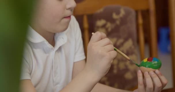 Een jongen schildert een paasei met een borstel — Stockvideo