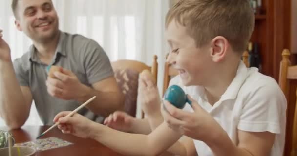 De vader met zijn twee kinderen kleurt paaseieren glimlachend breed — Stockvideo