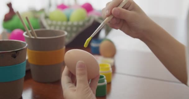 Macro, een kinderhand houdt een kippenei vast en begint het te schilderen. Voorbereiden op Pasen. Kinderen creativiteit, ambachten. Masterclass over het kleuren van eieren. Bovenaanzicht — Stockvideo