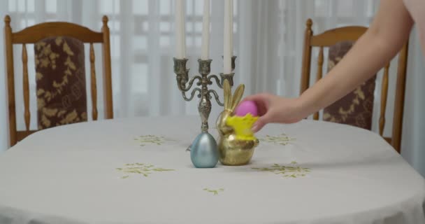 Жіночі руки розміщують на столі опору з рожевим пофарбованим яйцем. стіл для великодніх свят . — стокове відео