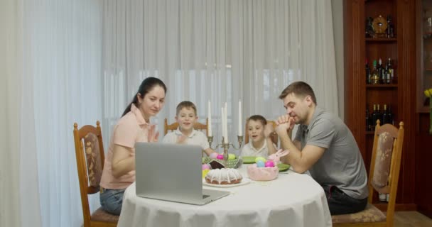 Ouders met twee tienerjongens praten over videogesprekken met een laptop, surfen op online tv-streams, genieten van tijd samen doorbrengen in het weekend, thuis, aan de vakantietafel voorbereid voor Pasen — Stockvideo